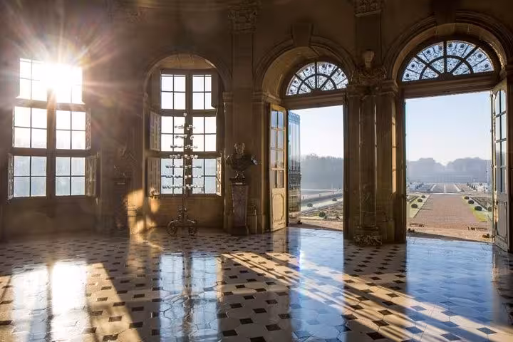 Sunlit grand hall with checkered marble floors and open doors overlooking Versailles gardens