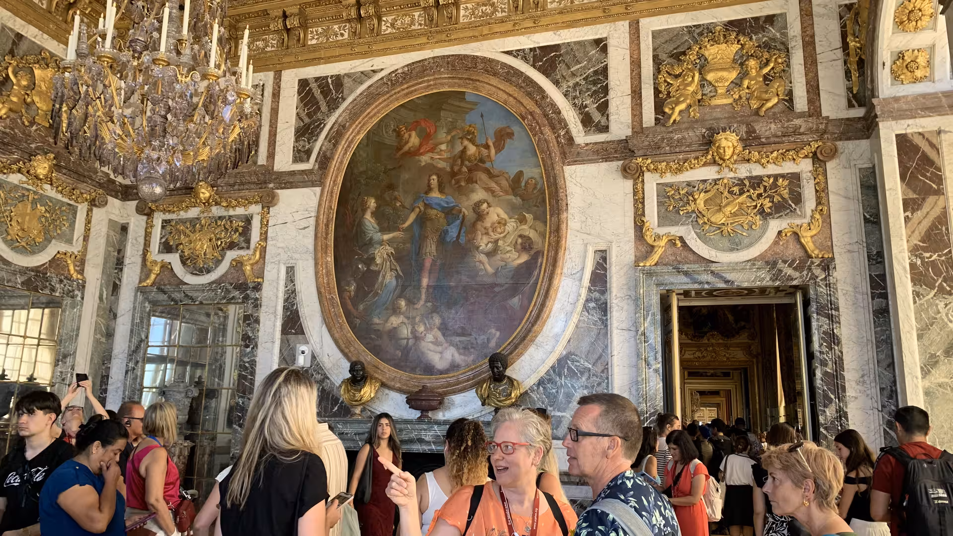 Tourists exploring ornate gilded Hall of Mirrors at Palace of Versailles with baroque ceiling paintings
