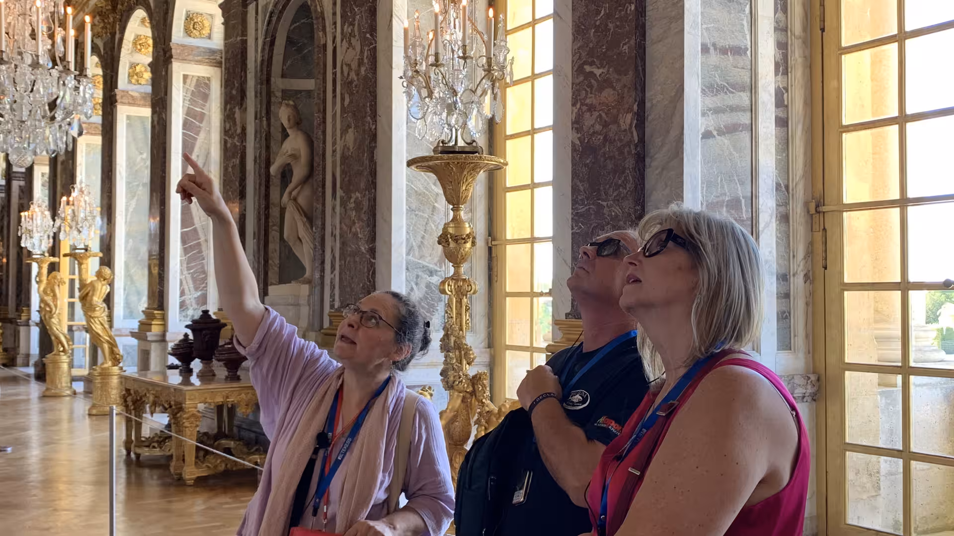 Tour guide pointing at ceiling details in the Hall of Mirrors at Palace of Versailles with visitors