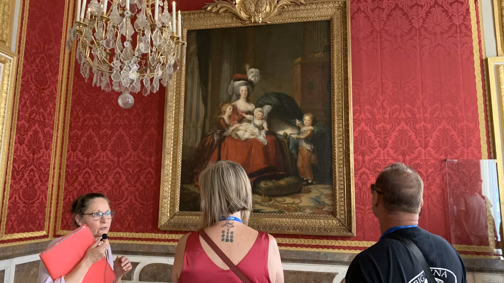 Tour guide explaining Marie Antoinette family portrait to visitors in ornate red room at Versailles Palace