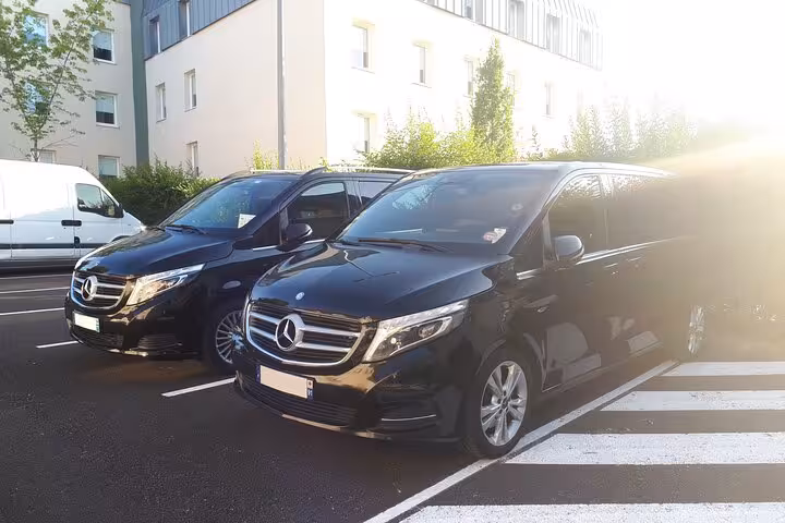 Two black Mercedes-Benz V-Class vans parked outside a building for private airport transfer service