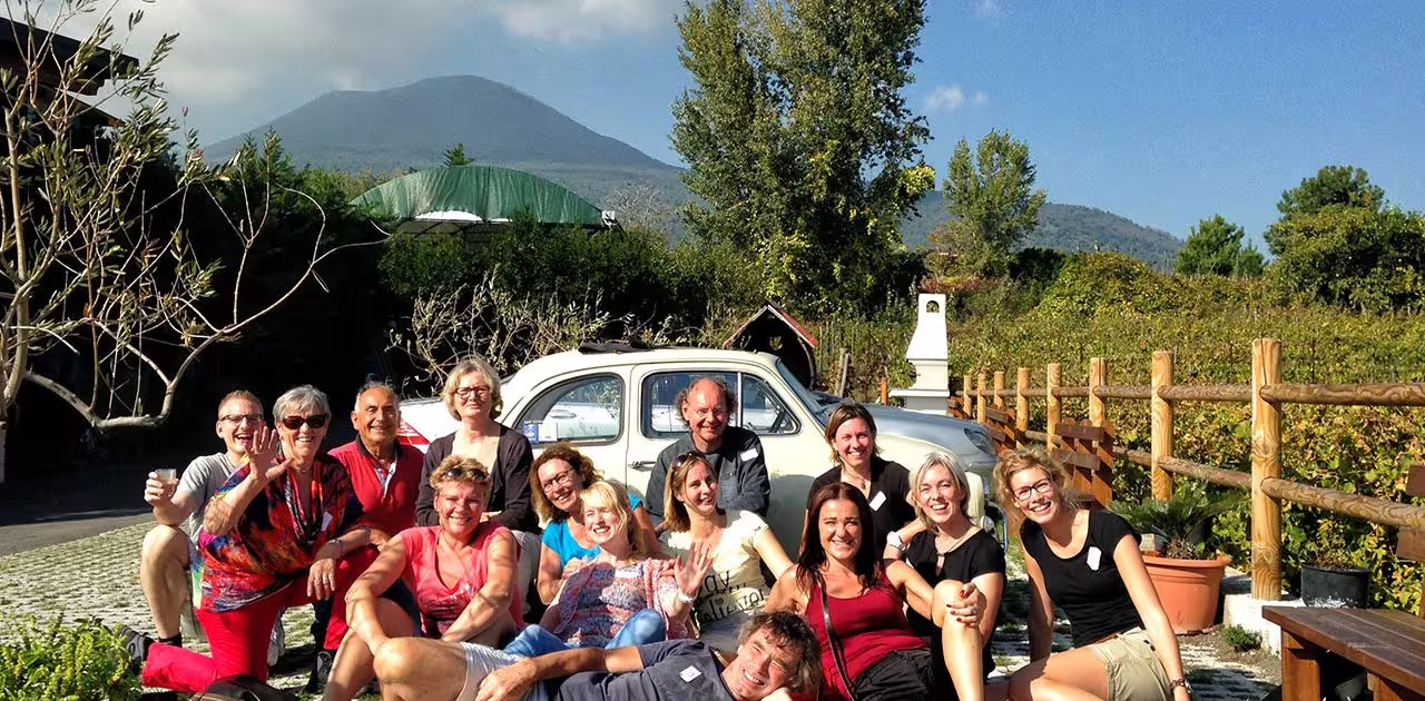 Happy group of travelers relaxing by a vintage car in a Vesuvius vineyard before their sunset dinner and wine-tasting experience