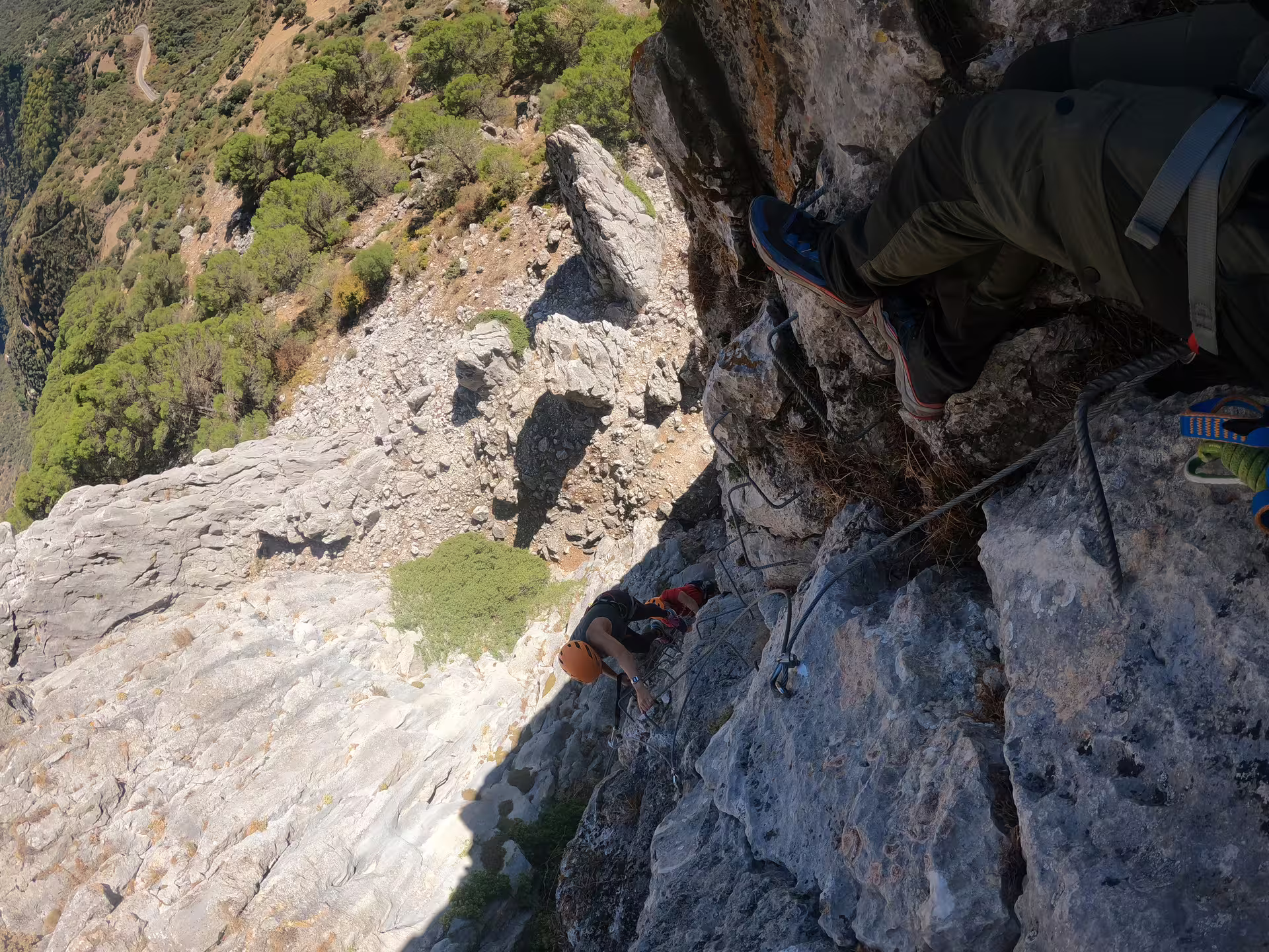Adventurer in helmet clings to sheer limestone cliff on guided Via Ferrata Benadalid tour overlooking dramatic Costa del Sol landscape