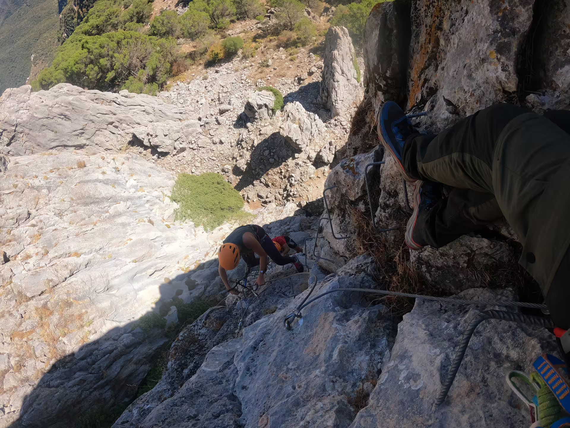 Climbers with helmets navigate fixed cable route on Via Ferrata Benadalid vertical rock face with scenic Andalusia valley below