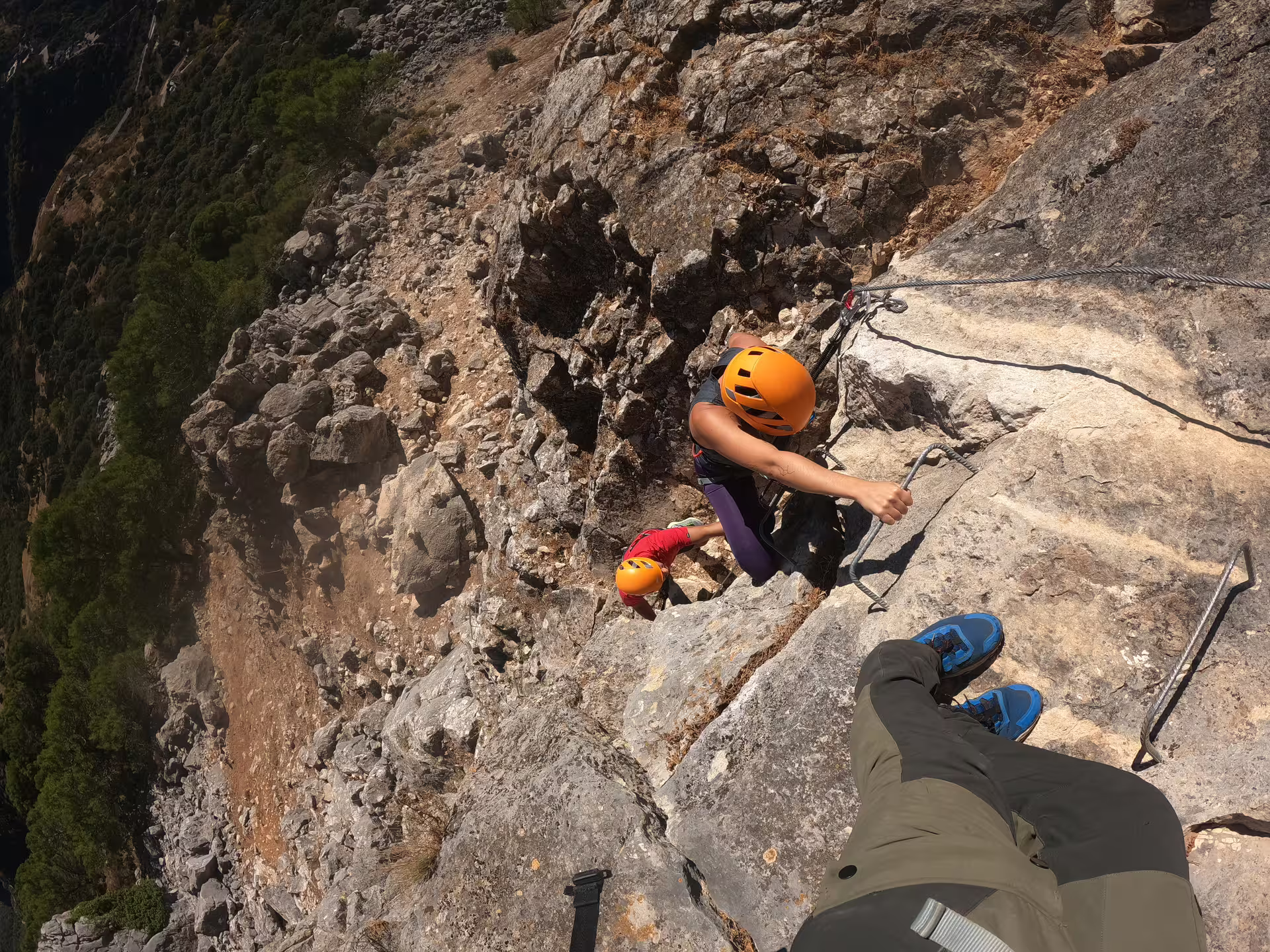 Adventurers climbing a rugged Via Ferrata route in Benalauría, equipped with safety gear against a stunning Costa del Sol backdrop.