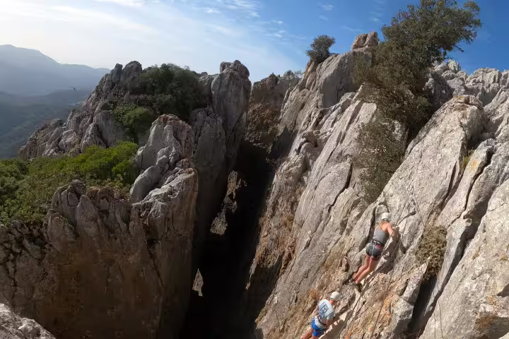 Adventurers scaling a rugged cliff on the Via Ferrata in Benalauría with breathtaking views of Costa del Sol's landscape.