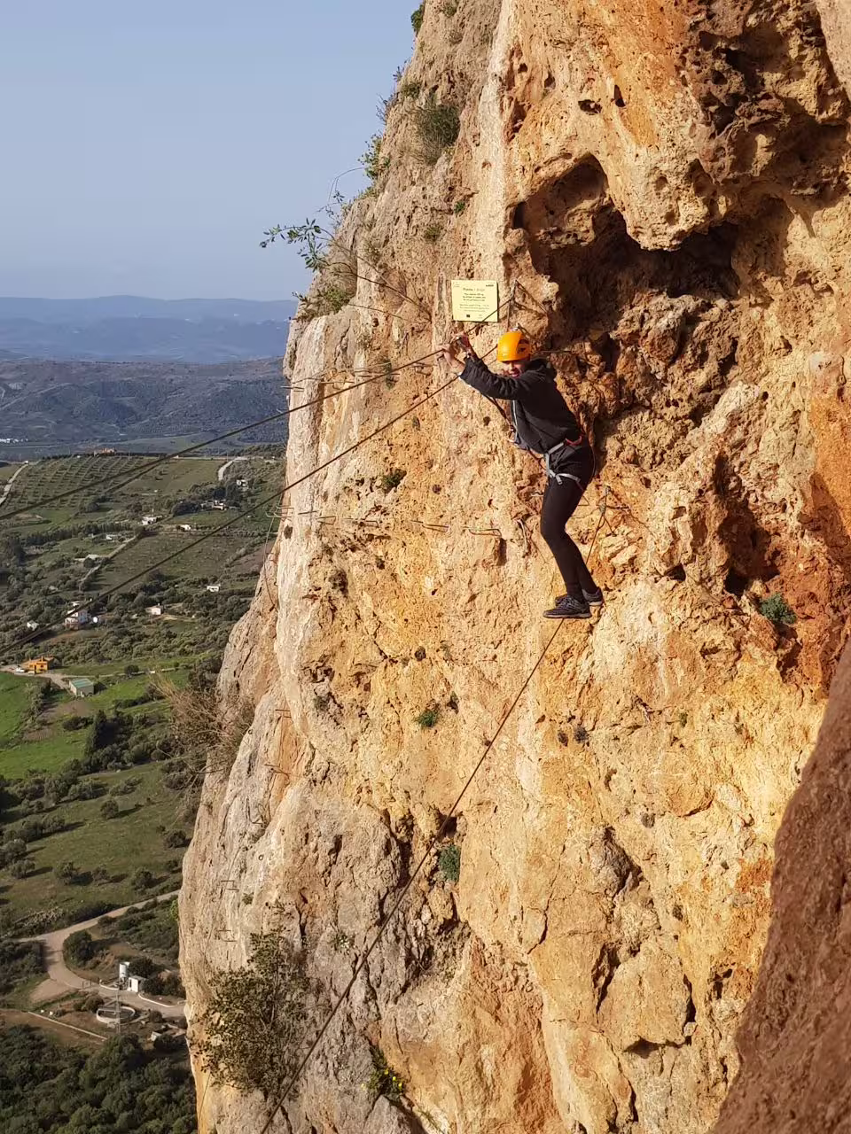 A helmeted climber scales a steep rocky cliff on the Via Ferrata Casares aerial climbing tour with scenic valley views