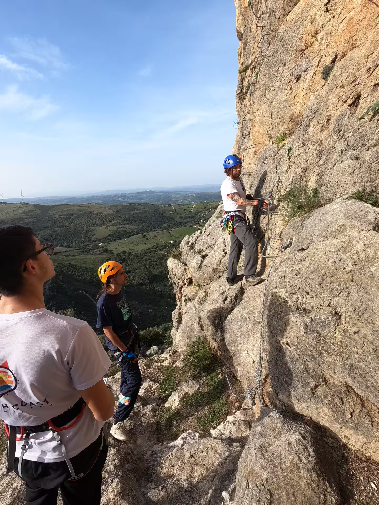 Climbers wearing helmets and harnesses prepare for an exciting Via Ferrata ascent on a rocky cliff in Casares.