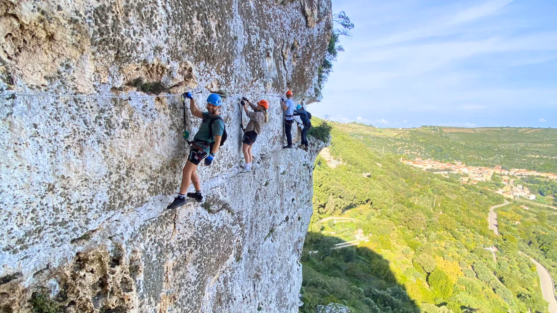Adventurers climbing the Via Ferrata di Giorré cliffside with scenic Cargeghe landscape in the background.