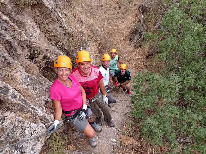 Group of smiling climbers wearing helmets navigating rocky via ferrata trail during guided tour in Ronda Spain