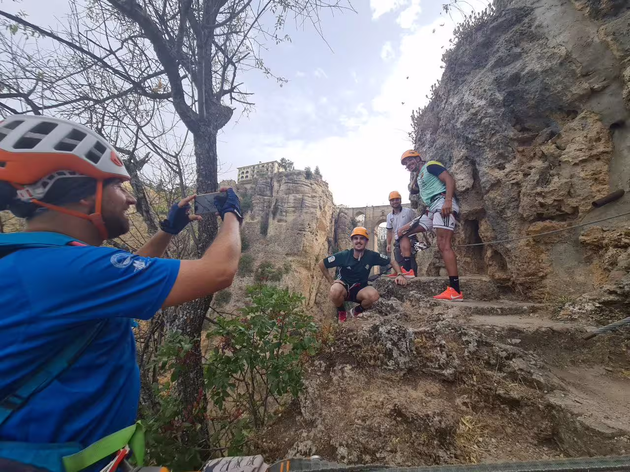 Guide photographing helmeted climbers on via ferrata route with iconic Ronda bridge and gorge cliffs in background