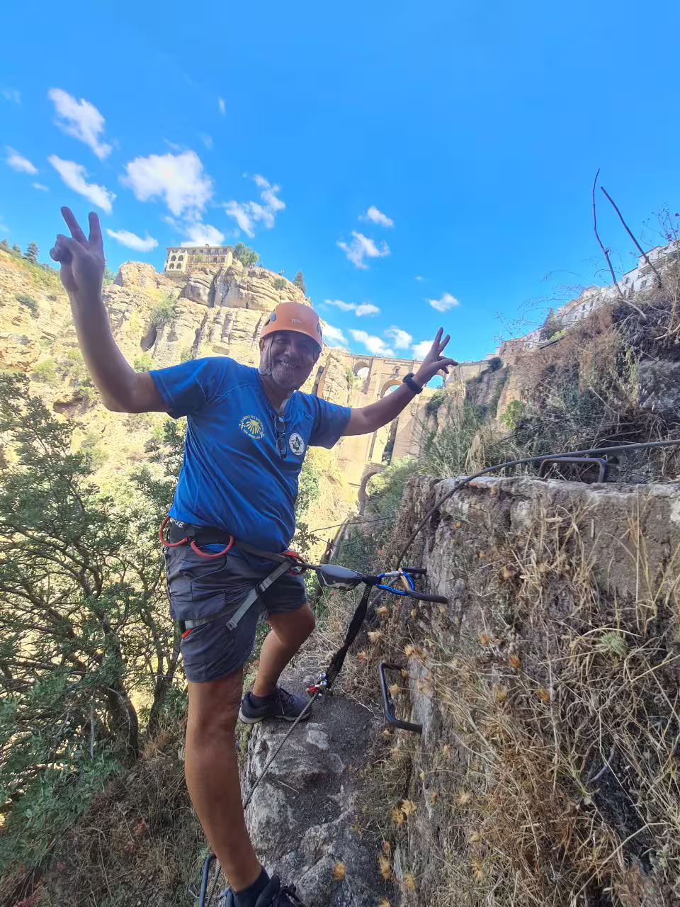 Happy climber in helmet celebrating on via ferrata route with iconic Ronda bridge and gorge in background
