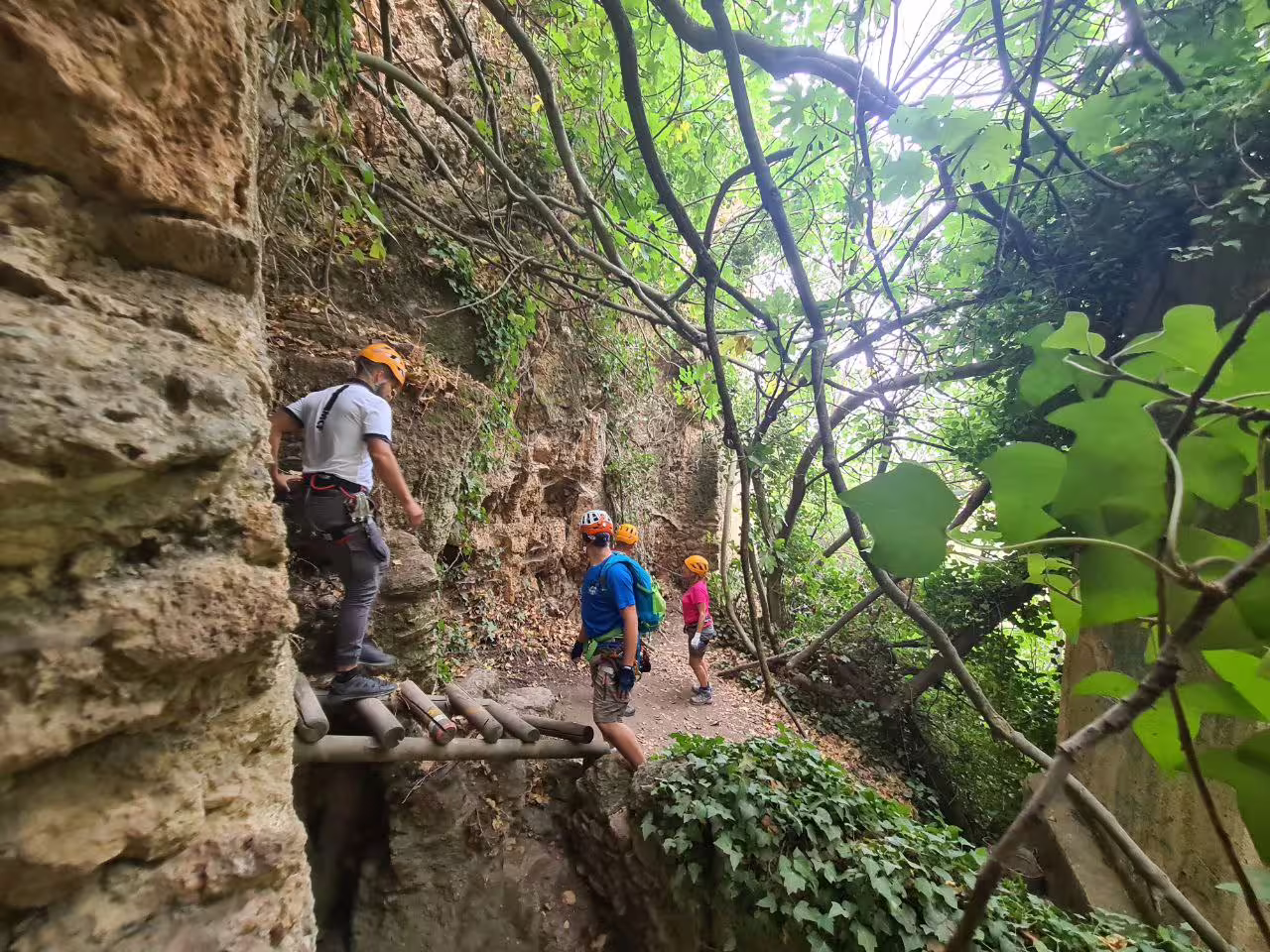 Three helmeted climbers navigate a wooden ladder bridge along rocky via ferrata trail in Ronda gorge