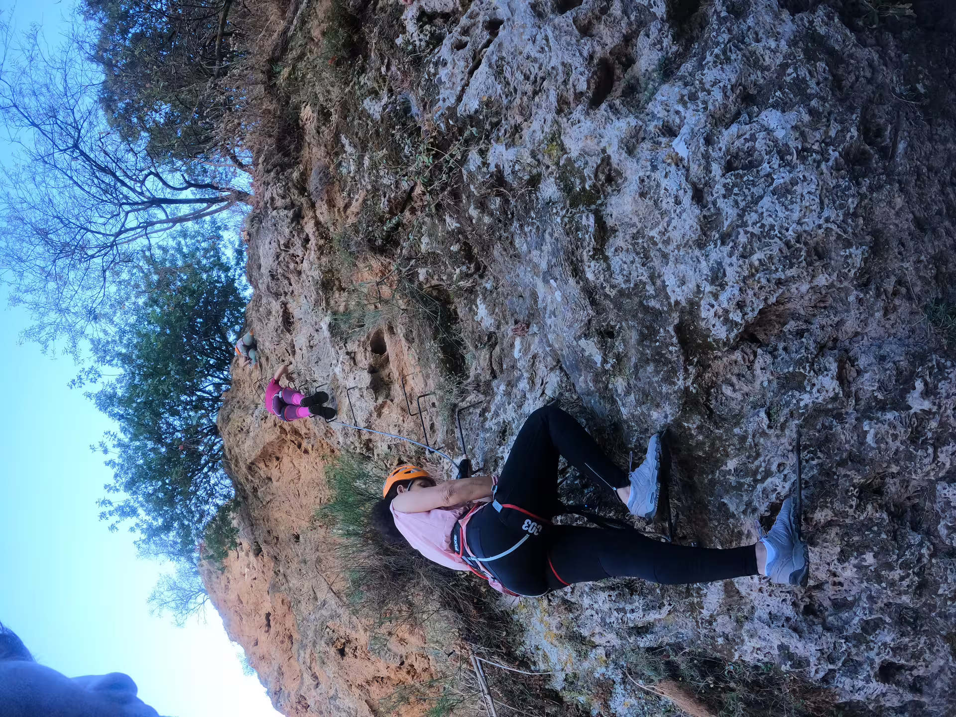 Harnessed climber in orange helmet navigating steep rock face during via ferrata guided tour in Ronda Spain