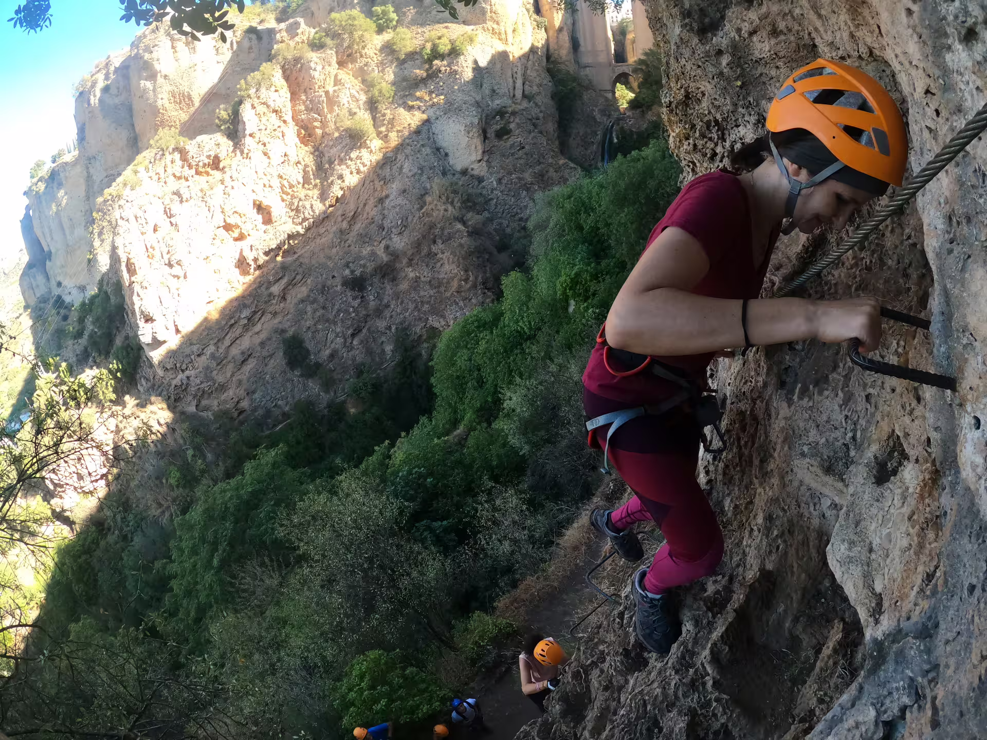 Climber in orange helmet scaling Tajo de Ronda cliff face on a guided via ferrata tour in Ronda Spain