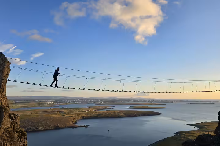 Person walking a suspension rope bridge high above Icelandic fjords near Reykjavik on Falcon Rock via ferrata