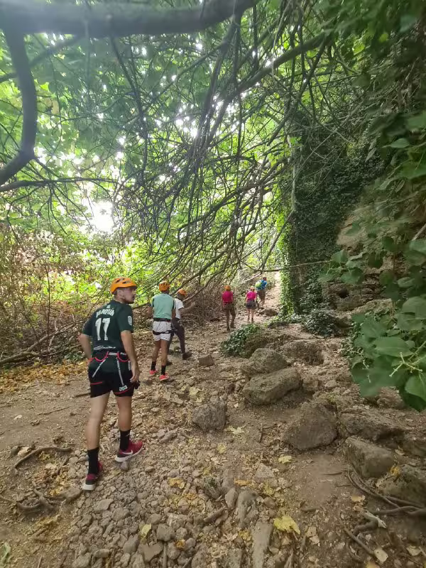 Adventure seekers navigate a lush, rocky path on the Via Ferrata Tajo de Ronda climbing experience.