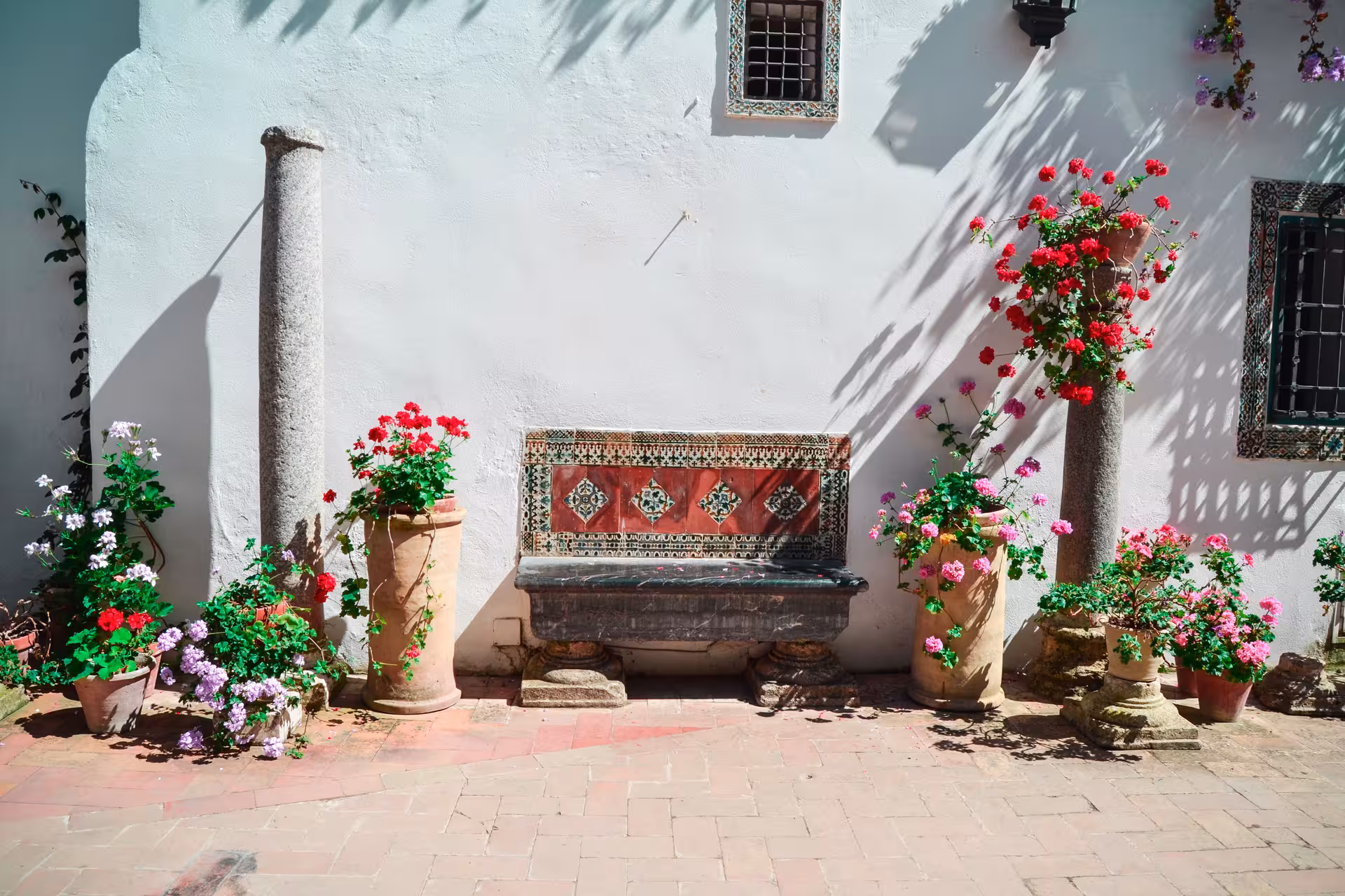 Discover a serene courtyard at Viana Palace adorned with colorful flowers and traditional Spanish tiles.