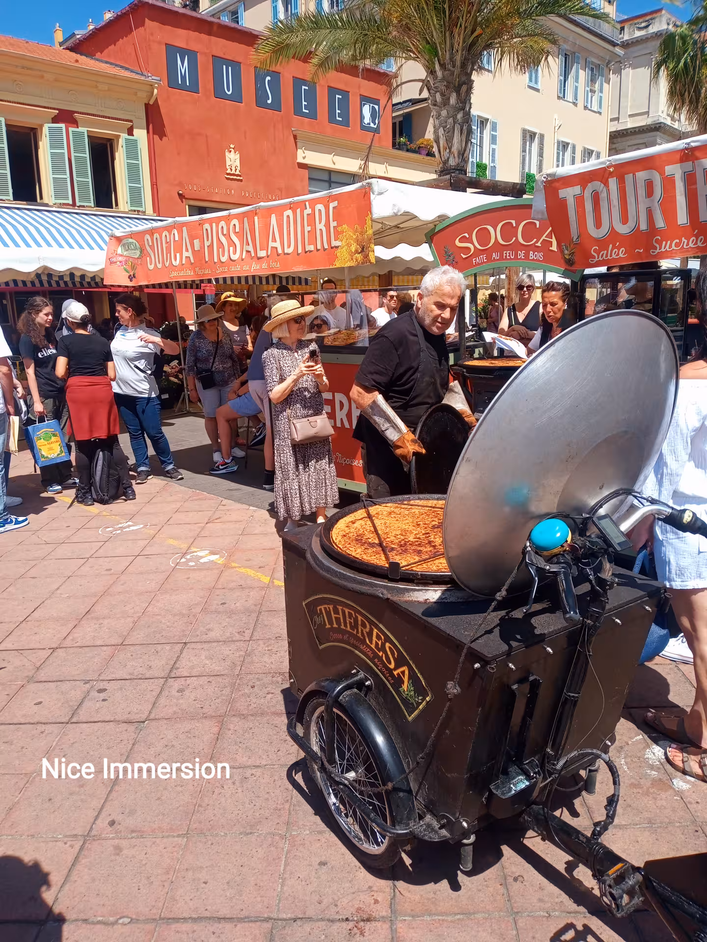 Experience vibrant local culture at a bustling street market in Nice, featuring traditional socca stalls and lively crowds.