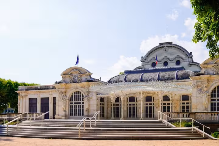 Grand ornate Belle Époque building with French flags and glass canopy entrance in Vichy, France