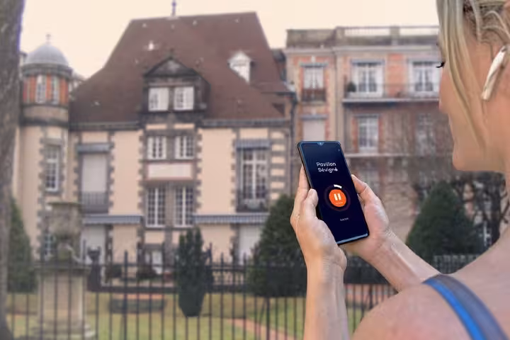 Woman holding smartphone with GPS audio guide app in front of Pavillon Sévigné in Vichy, France