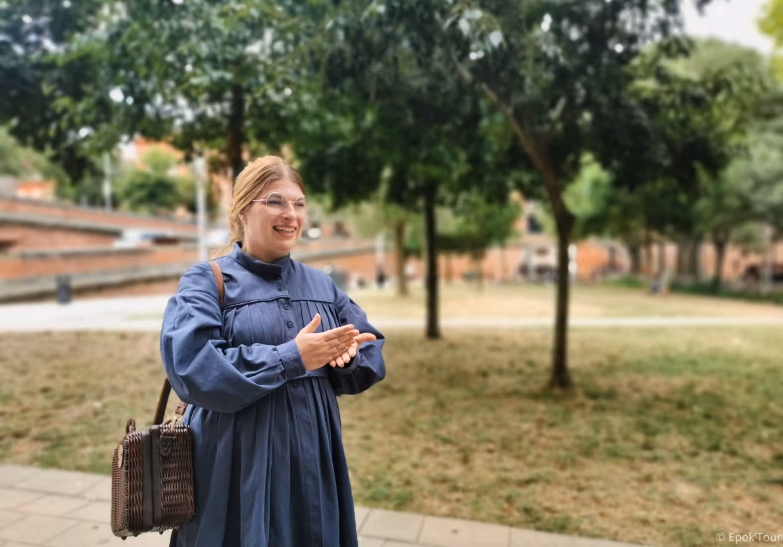 Smiling female guide in blue Victorian dress holding wicker bag during outdoor tour of Toulouse