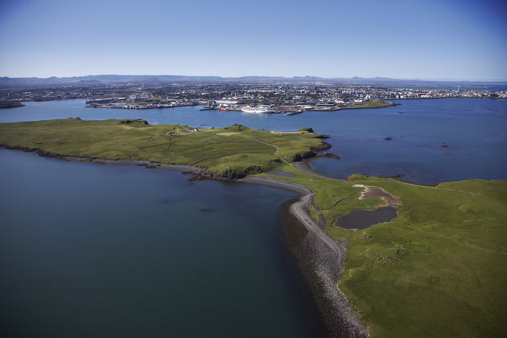 Aerial view of Videy Island with green hills and Reykjavik city harbor in the background