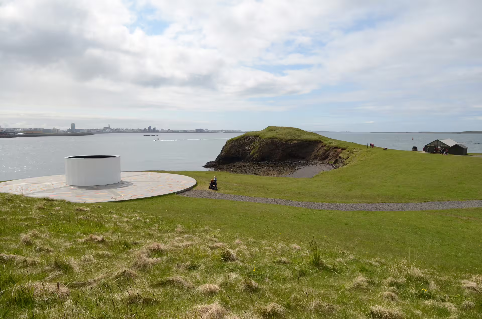 Videy Island green coastal landscape with circular sculpture, rocky cliffs, and Reykjavik skyline across the bay