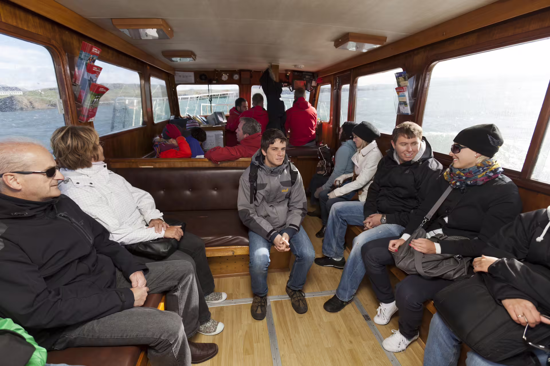 Tourists seated inside Videy Island ferry cabin with ocean views through windows near Reykjavik