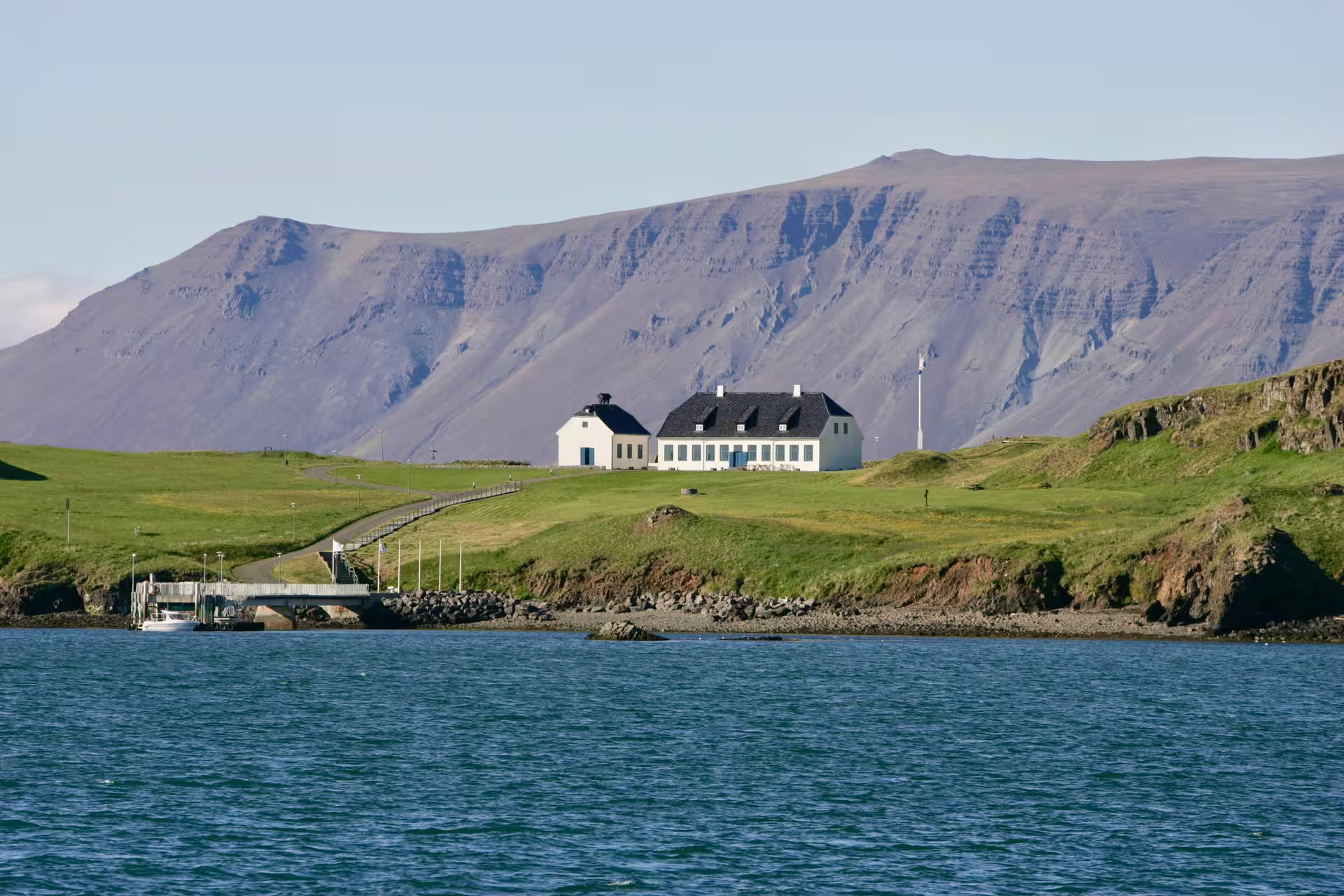 Videy Island white building on green hillside with dramatic mountain backdrop and ferry dock in Reykjavik