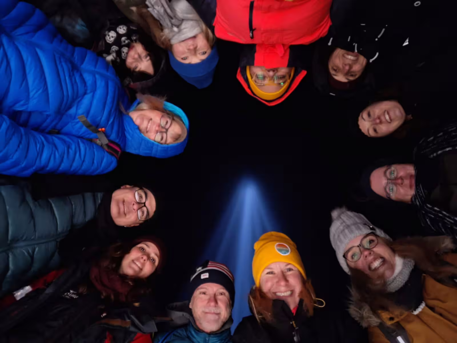 Group of tourists in winter gear forming a circle around Imagine Peace Tower light beam on Videy Island at night