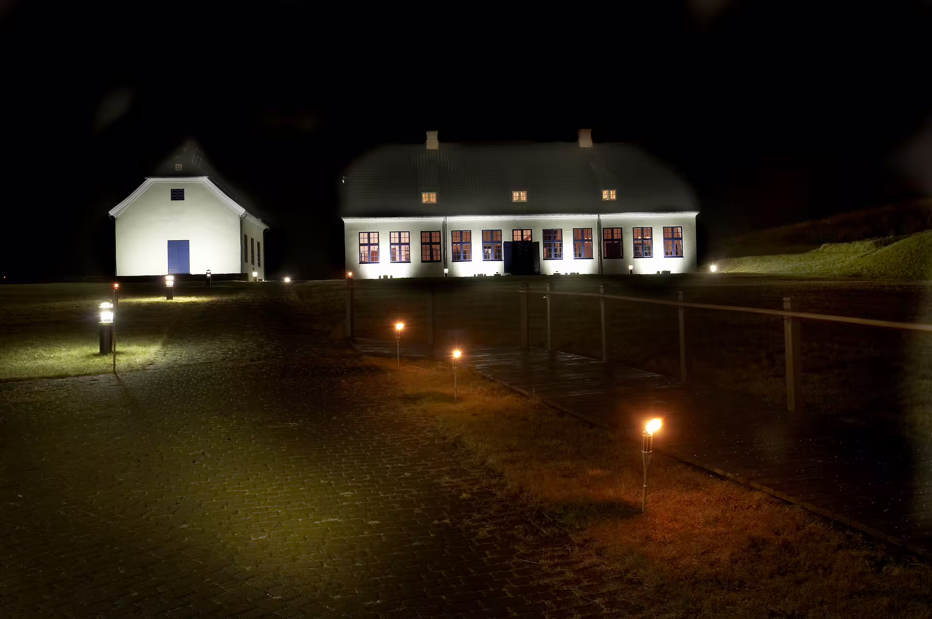 Videy Island historic white buildings illuminated at night with torches lining the cobblestone path