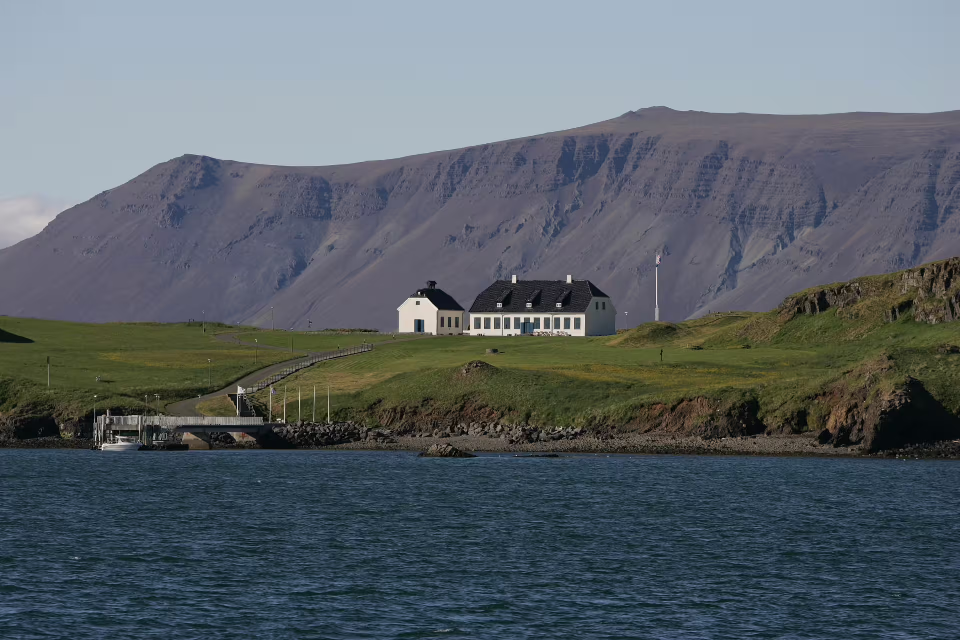 Videy Island historic white buildings on green hillside with dramatic mountain backdrop viewed from Reykjavik harbour