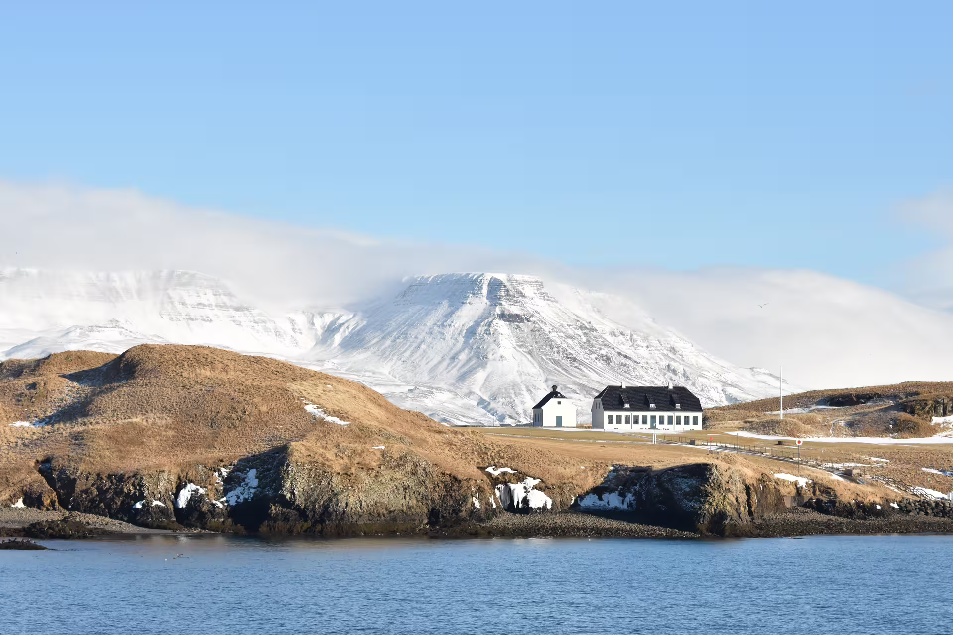 Videy Island white building with snow-capped mountains and calm blue waters in Reykjavik winter