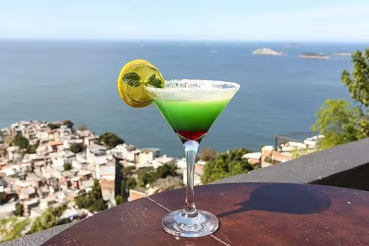 A vibrant cocktail with a scenic view of Vidigal Favela and the ocean, part of the Hike Two Brothers Hill experience.