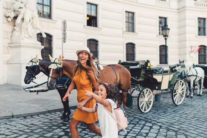 Mother and daughter joyfully explore Vienna's historic streets with a horse-drawn carriage on a family-friendly private tour.