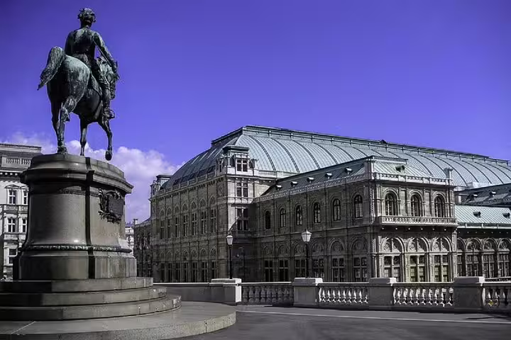 Equestrian statue in front of the Vienna State Opera building under a clear blue sky