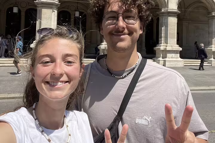 Two smiling tourists taking a selfie during a walking tour in Vienna with historic architecture in background