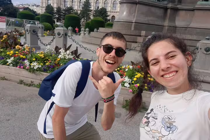 Two smiling tourists on a self-guided walking tour in Vienna with colorful flowers and historic building behind them