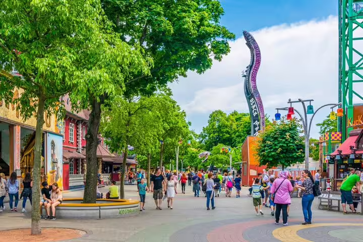 Visitors strolling through Vienna Wurstelprater amusement park with colorful rides and tree-lined promenade