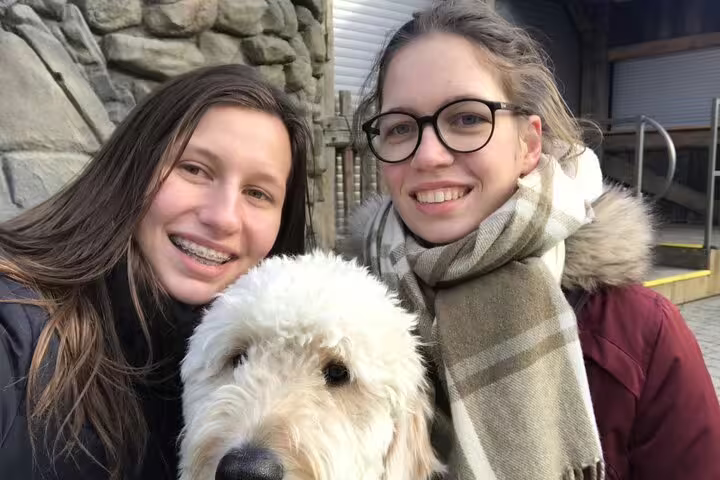 Two smiling women posing with a fluffy white dog outdoors at Vienna Wurstelprater