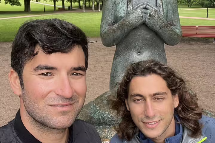 Two men smiling in front of a bronze sculpture at Vigeland Park, Oslo