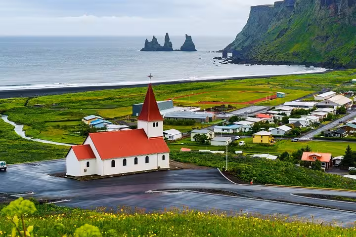 Vík í Mýrdal church with red roof overlooking black sand beach and Reynisdrangar sea stacks, Iceland South Coast