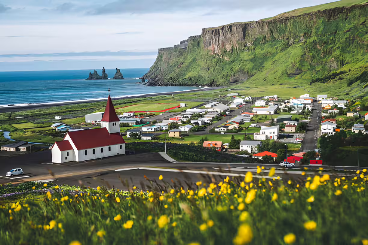 Panoramic view of Vík village with red-roofed church, black sand beach, and Reynisdrangar sea stacks, Iceland