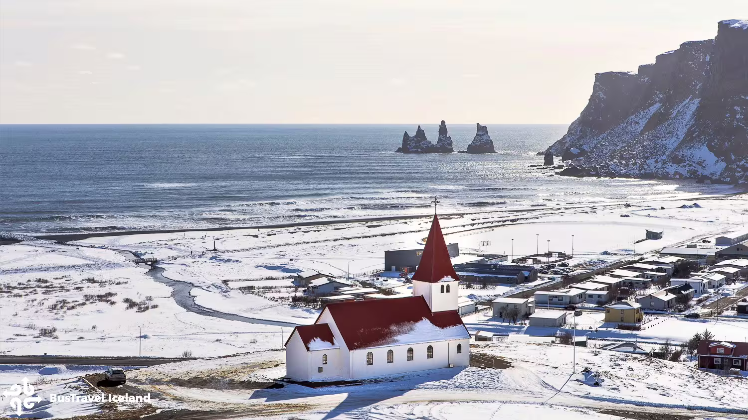 Vík church with red roof overlooking black sand beach and Reynisdrangar sea stacks in winter, Iceland