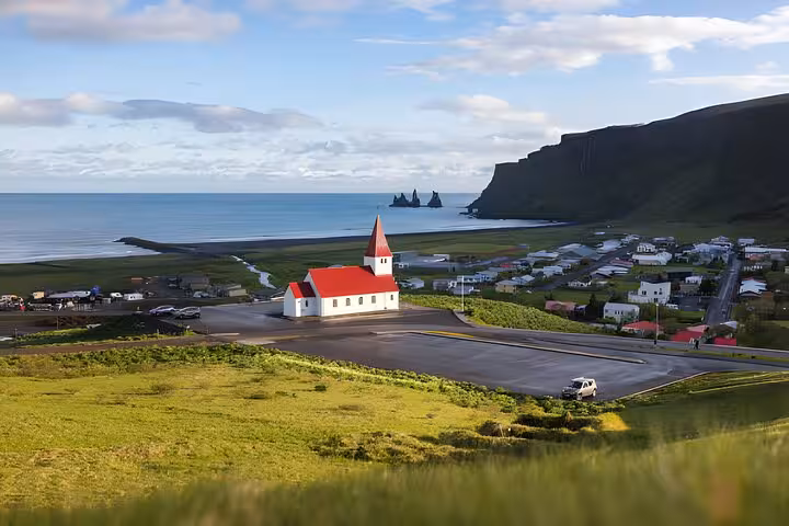 White church with red roof overlooking Vik village, black sand beach, and dramatic sea stacks on Iceland's South Coast