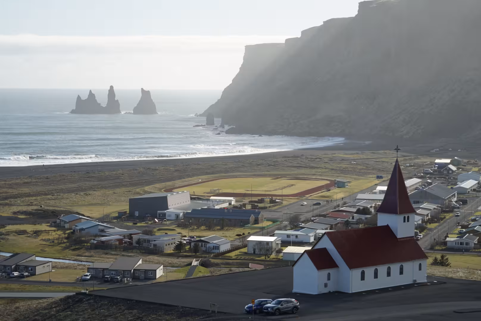 Vík í Mýrdal village church with black sand beach, Reynisdrangar sea stacks, and dramatic cliffs on Iceland's South Coast