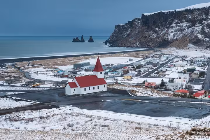 Aerial view of Vík village with red-roofed church, black sand beach, and Reynisdrangar sea stacks in winter, Iceland