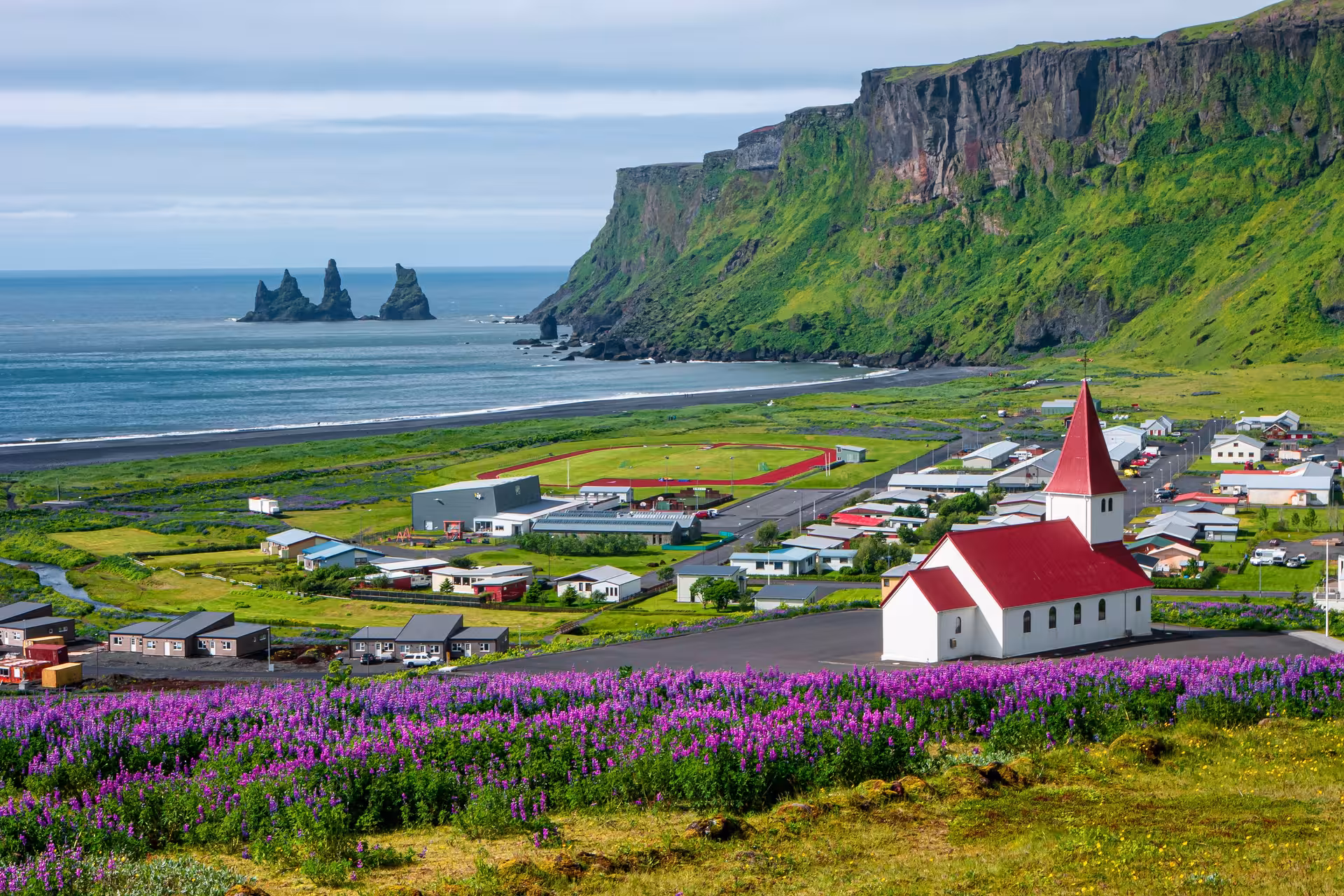 Scenic view of Vik village with Reynisdrangar sea stacks and lush green cliffs along Iceland's South Coast.