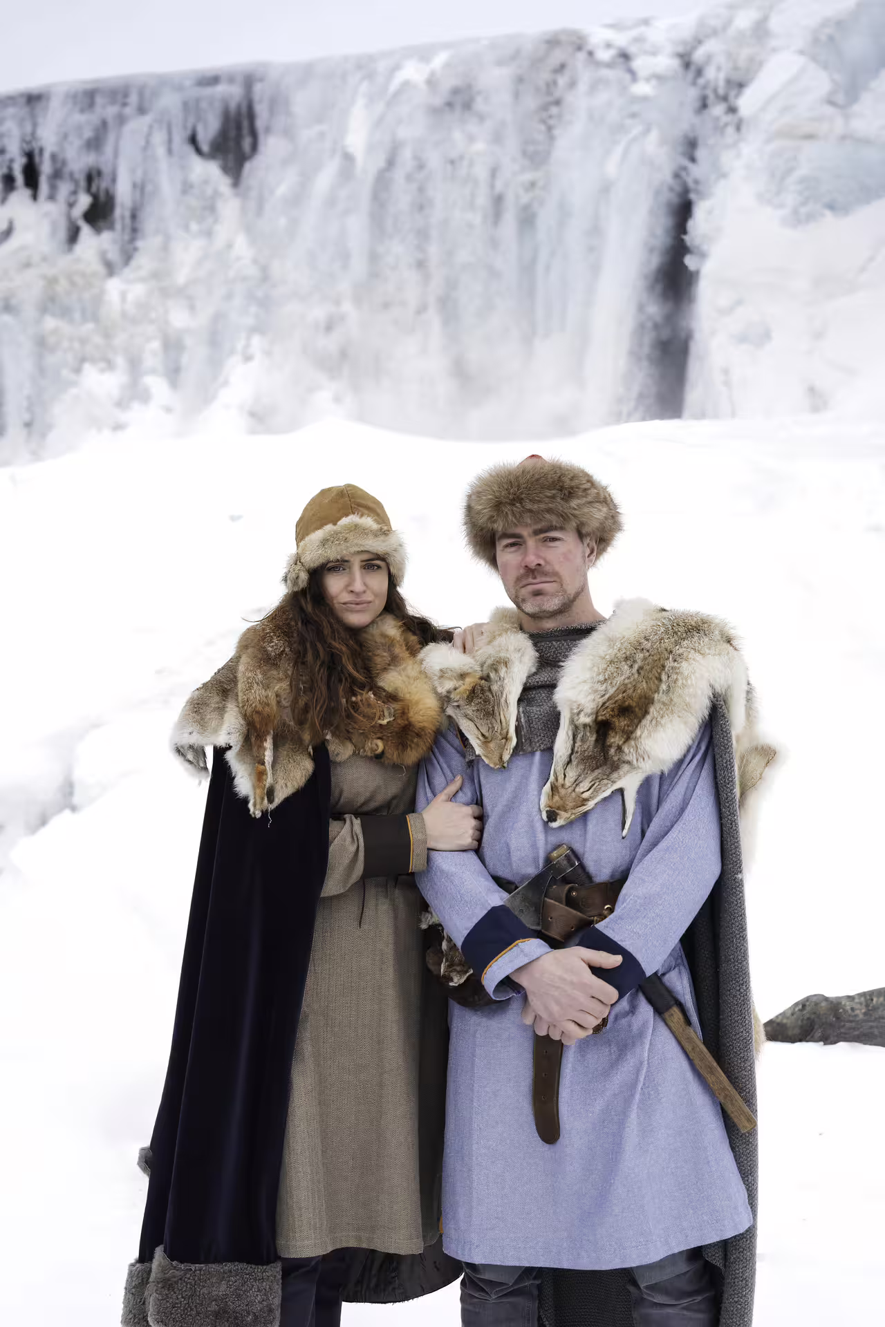 Couple in authentic Viking costumes with fur pelts and axe posing before a frozen Iceland waterfall on circle tour